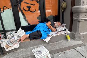 Man sleeps in a building entrance on newspapers in the morning in the commercial district of the Park Slope neighborhood of Brooklyn, New York on a summer morning.