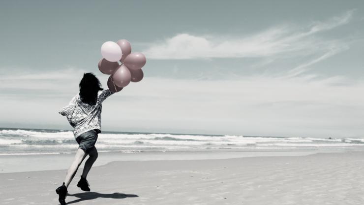 Žena trči na plaži s balonima