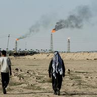 FILE PHOTO: People walk near farmland by the Zubair oil field as gas flares rise in the distance, in Zubair Mishrif, Basra