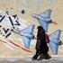 An Iranian woman walks past an anti-Israeli mural in Tehran
