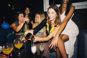 A lively group of young women enjoying a night out at a night club, sharing laughter and pouring champagne.
