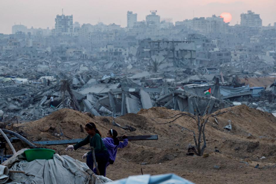FILE PHOTO: A Palestinian child holds a piece of wood with the rubble of destroyed buildings in the background, amid a ceasefire between Israel and Hamas, in Jabalia | Author: Mahmoud Issa