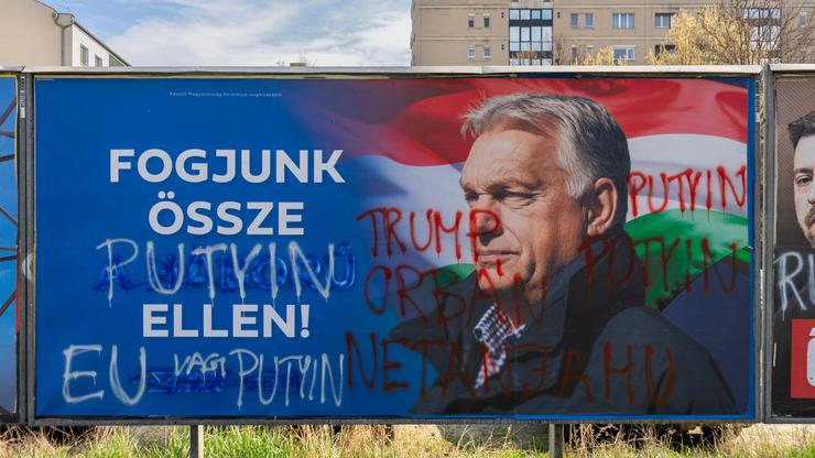 Defaced Fidesz billboard with anti-war slogan and graffiti referencing Putin and Trump in Budapest during Hungary’s 2026 election campaign.