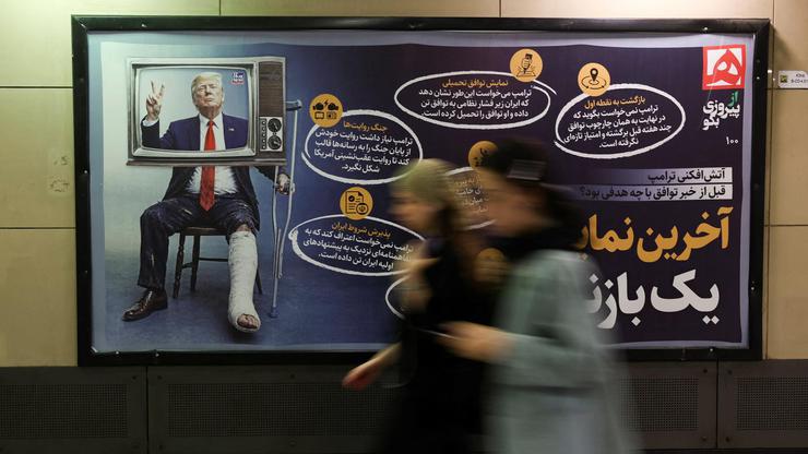 People walk past a sign with a picture depicting injured U.S. President Donald Trump, in Tehran