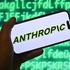 Hand shows a smartphone with the Anthropic logo in front of a computer background