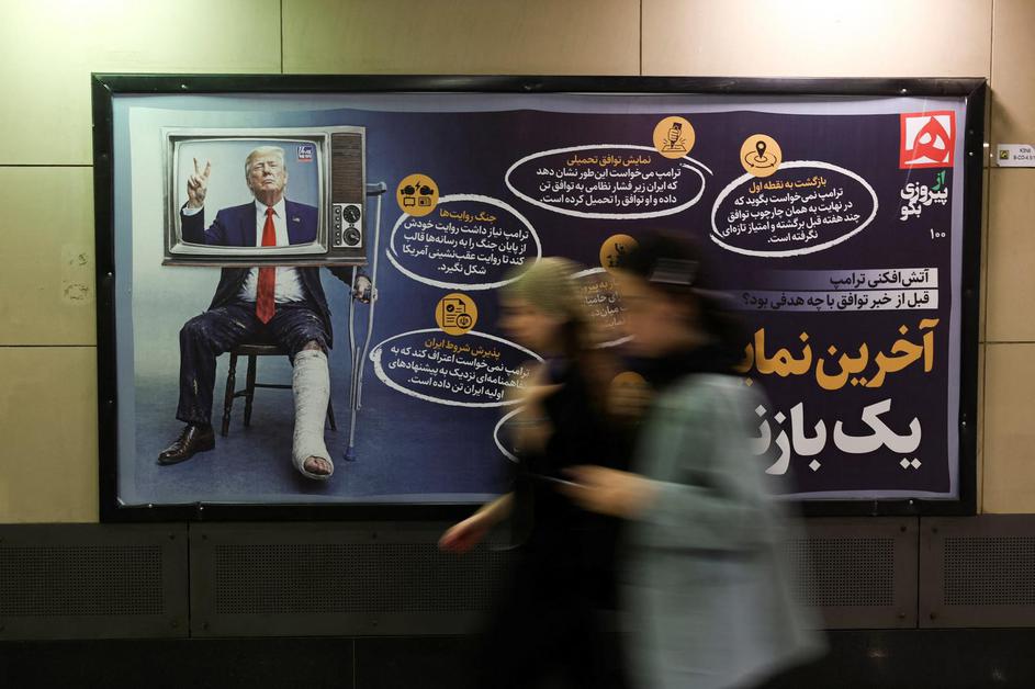 People walk past a sign with a picture depicting injured U.S. President Donald Trump, in Tehran