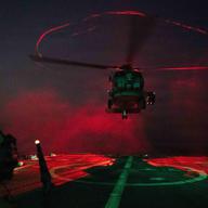 Undisclosed Location, United States. 18 March, 2026. A U.S. Navy sailor signals a MH-60S Sea Hawk helicopter, attached to the Chargers of Helicopter Sea Combat Squadron 14, to take off during night operations on the deck of the Arleigh Burke-class guided-