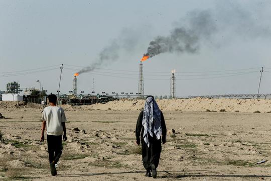 FILE PHOTO: People walk near farmland by the Zubair oil field as gas flares rise in the distance, in Zubair Mishrif, Basra
