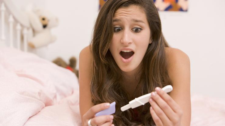 Žena iznenađeno gleda rezultate testa na trudnoću