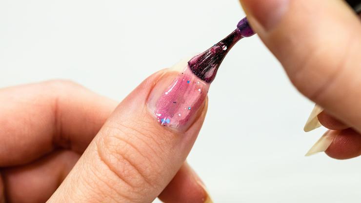 Female hands doing manicure, nail polish in gold glitter color on a white background. Skin and nail care salon concept