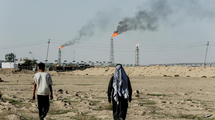 FILE PHOTO: People walk near farmland by the Zubair oil field as gas flares rise in the distance, in Zubair Mishrif, Basra