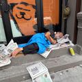 Man sleeps in a building entrance on newspapers in the morning in the commercial district of the Park Slope neighborhood of Brooklyn, New York on a summer morning.