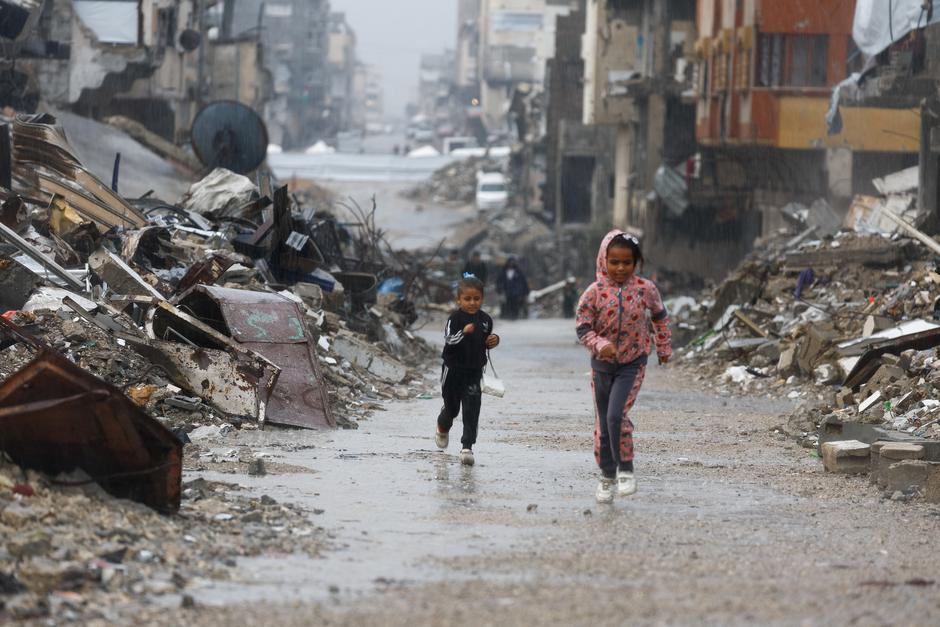 Palestinian children run next to piles of rubble and damaged buildings, during a rainy day in Gaza City | Author: Mahmoud Issa