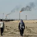 FILE PHOTO: People walk near farmland by the Zubair oil field as gas flares rise in the distance, in Zubair Mishrif, Basra